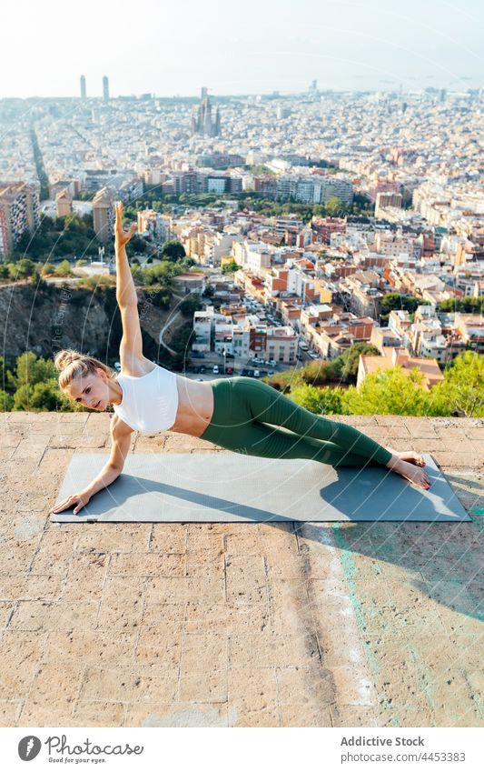 Slim woman performing Side Forearm Plank pose on rooftop side forearm plank yoga balance support arm raised healthy lifestyle vitality energy city wellness town