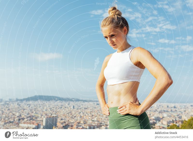 Sportswoman contemplating city under cloudy sky athlete cityscape hand on waist district healthy lifestyle thoughtful break sportswoman town pensive atmosphere