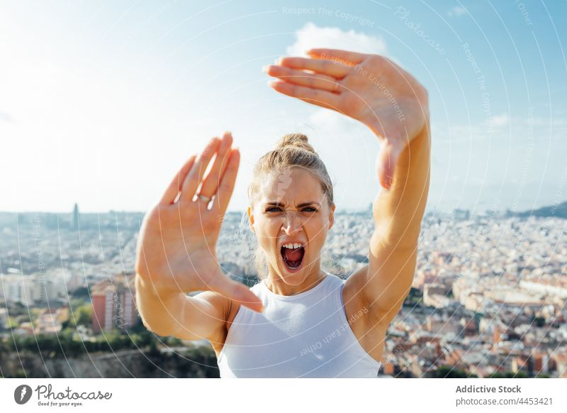 Sportswoman screaming while showing frame gesture during workout in city sportswoman shout angry aggressive rage photo town portrait anger yell mouth opened