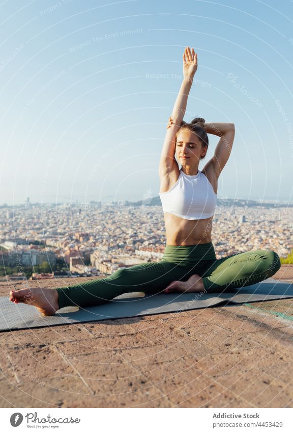 Woman stretching arm on yoga mat in town woman healthy lifestyle wellness vitality rooftop blue sky city pose practice wellbeing energy sportswear barefoot fit