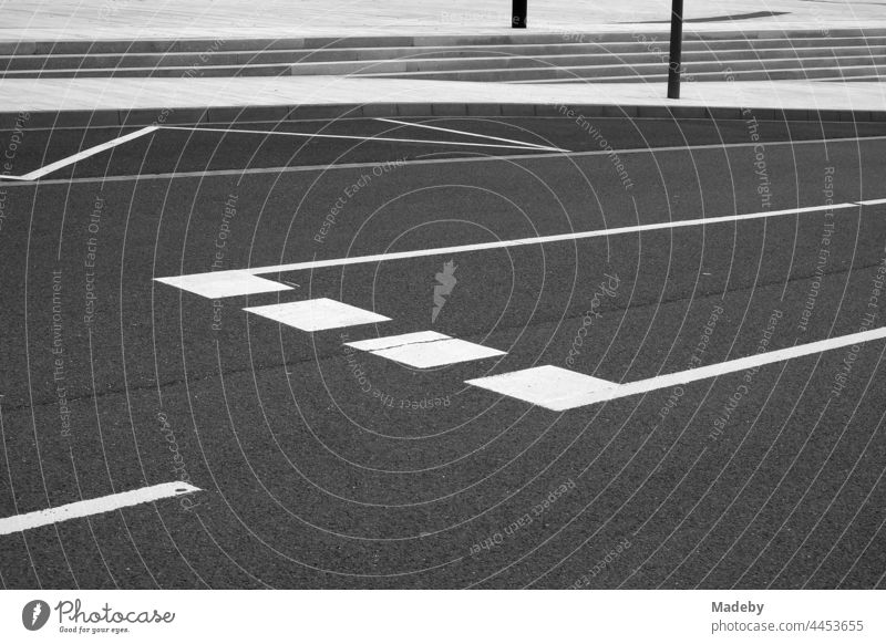 White road markings on dark asphalt with turning lane and bus stop at Leitz Park in Wetzlar on the Lahn in Hesse, photographed in classic black and white