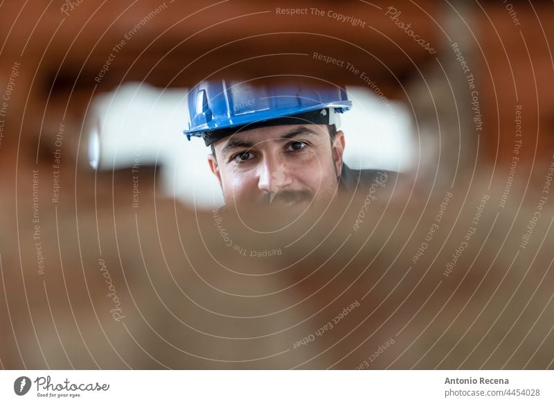 Worker during renovations looks through a hole through which the light switches will go picola profile man bricklayer worker job construction arab 40s persona