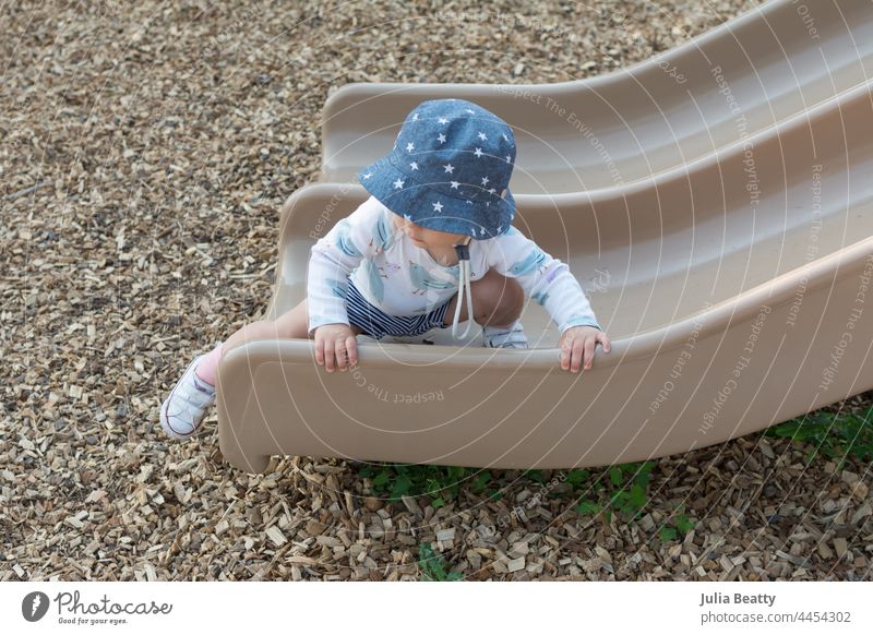 15 month toddler navigating the playground; child crawling on a slide using both hands to grip and pull pull up 15 months old baby learn learning hold reach