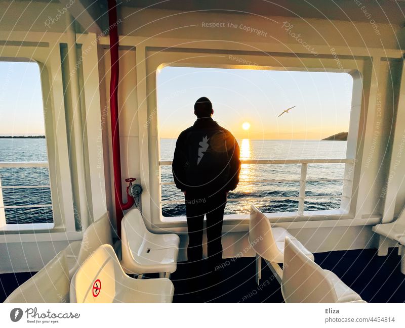 A man stands at the railing of a ferry and looks across the sea to the sunrise Ferry gulls Railing Man Observe Crossing Passenger ship Trip On board Ocean