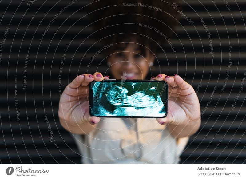 Smiling black woman showing smartphone screen with baby ultrasound pregnant using picture happy expect female belly pregnancy cellphone maternal motherhood