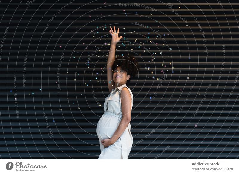 Happy black pregnant woman throwing confetti anticipate toss celebrate positive maternal await tummy female colorful glad pregnancy expect belly abdomen