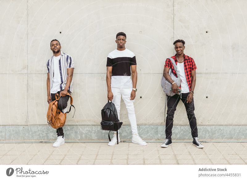Black male friends in stylish outfits standing near concrete wall men cool style masculine trendy modern confident individuality posture appearance together