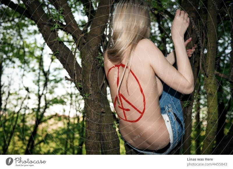 That’s what it's like to live in a tree. Like this naked gorgeous blonde girl is doing. Climbing tree branches, with blue jeans only, and a red devil’s sign on her sexy back. Wild blood mixed with a perfect summer’s weather out in the woods.