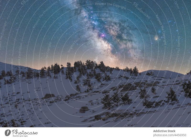 Snowy mountains under starry sky with Milky Way snow slope nature rocky highland ridge landscape peak range hill picturesque tree cliff winter forest terrain