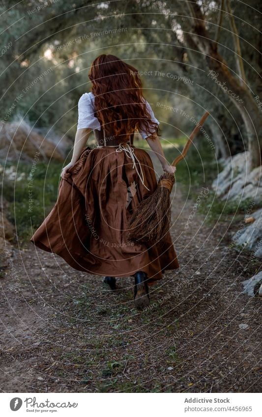 Witch with broom running in woods witch broomstick forest woman enchantress dark autumn female witchcraft magic mystic magician dull gloomy pathway halloween