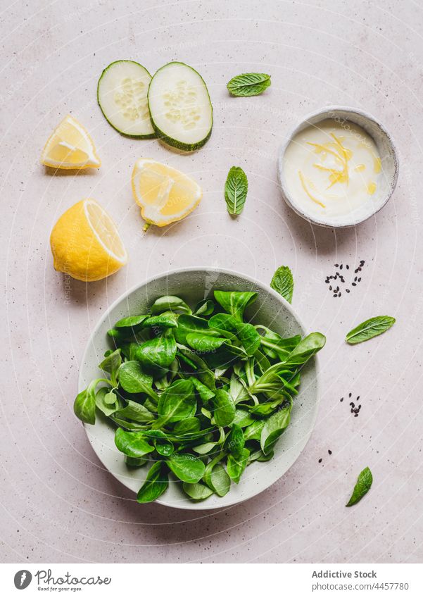 Assorted fresh ingredients and lemon sauce on gray background salad spinach mint cucumber sesame recipe culinary healthy food vitamin vegetable seed zest citrus