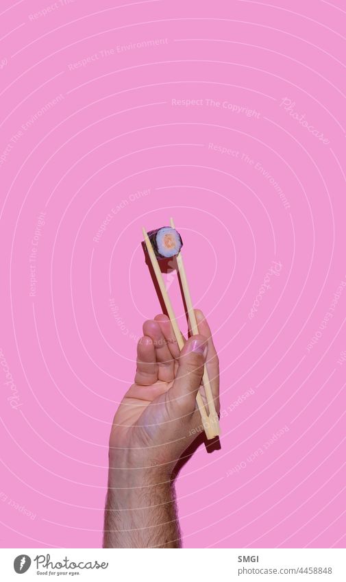 A man's hand holding sushi with Japanese chopsticks on pink background. Sushi and Japanese food concept japanese chinese oriental china restaurant isolated