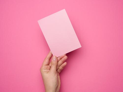 Female hand holding empty pink paper on a pink background. Copy paste image or text person blank business white card finger message communication showing sign