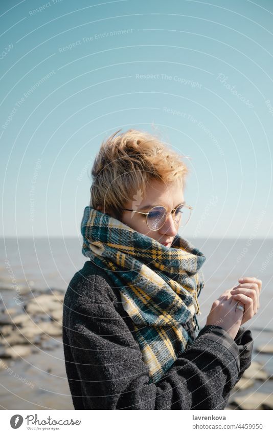 Young female in glasses warming herself on a beach alone autumn caucasian coat cold face fall hands lifestyle nature outdoors person portrait seaside sky travel