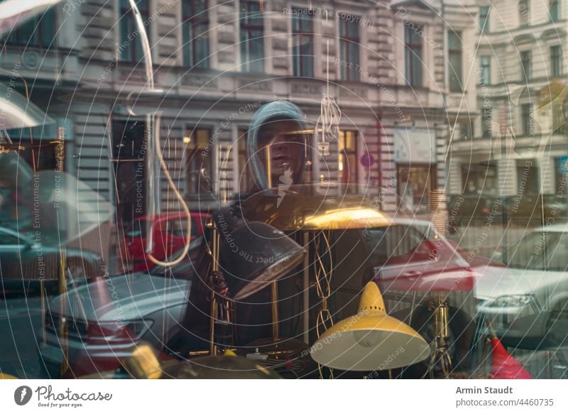 The reflection of a young man in a shop window with old lamps portrait hoodie street urban showcase second hand many multicolor glass city sell buy market