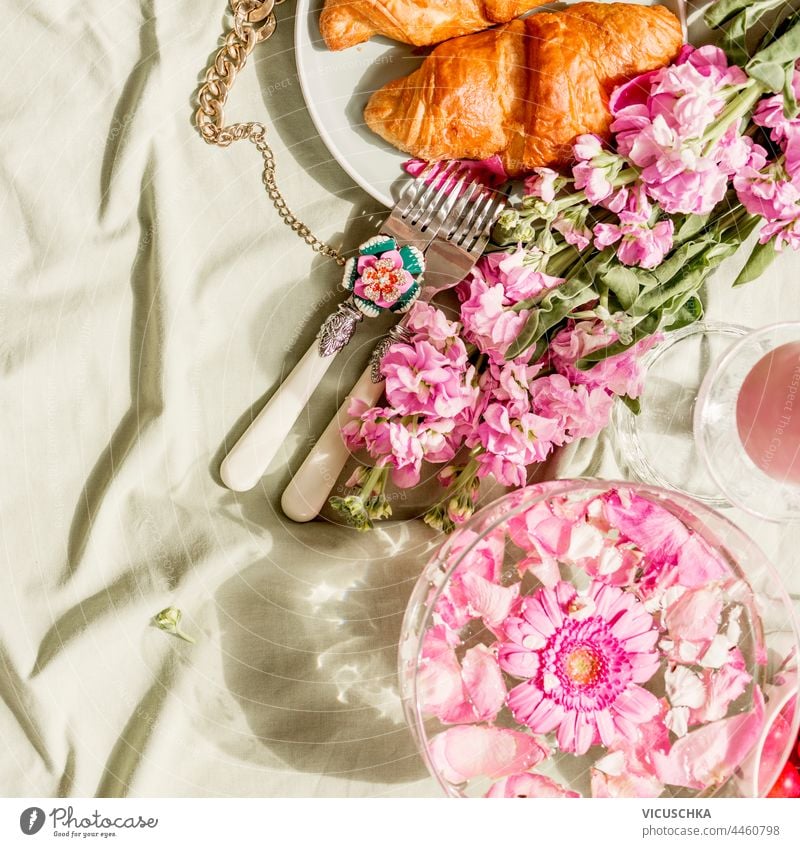 Aesthetic breakfast with croissant and pink flowers bunch on light green blanket at sunshine. Top view aesthetic top view above background fashion food fruits
