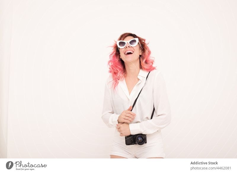 Cheerful woman in sunglasses standing with photo camera against light wall style trendy happy smile appearance cheerful positive female outfit room photographer