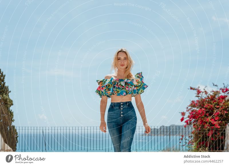 Stylish woman standing on roof of coastal house confident style sea feminine gentle carefree travel female modern jeans building shore water trendy nature