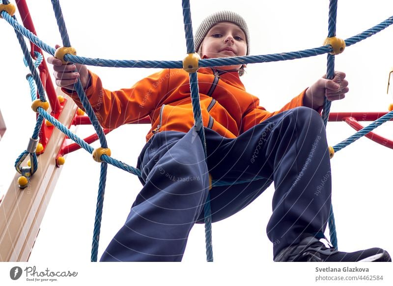 Funny caucasian blond boy in an orange jacket plays on the sports playground happy childhood outdoors teen kid smiling fun park playing school day schoolyard