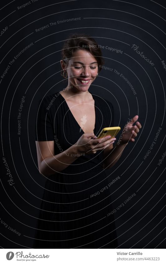A young beautiful woman using a smartphone in a studio shot in black dress and background 20-25 adult attractive beauty brunette casual close-up concepts
