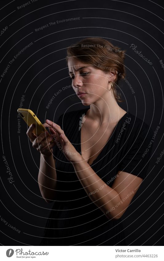 A young beautiful woman using a smartphone in a studio shot in black dress and background 20-25 adult attractive beauty brunette casual close-up concepts