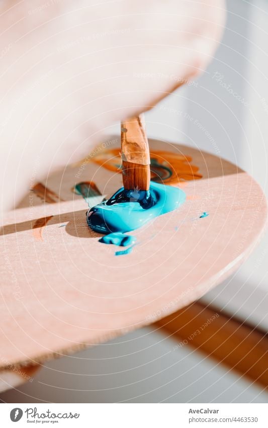 Close up of paintbrush picking blue color from an artist palette. Colorful image from an artist’s studio or a school showing creative education person woman