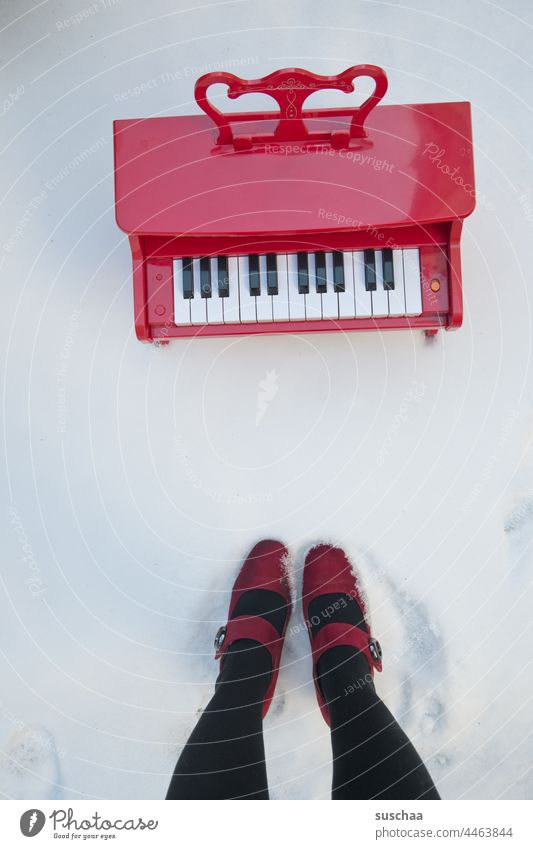 children piano in the snow, next to it legs of a lady Children's piano Red Snow Winter Cold red women's shoes High heels Legs feet standing quaint fumble
