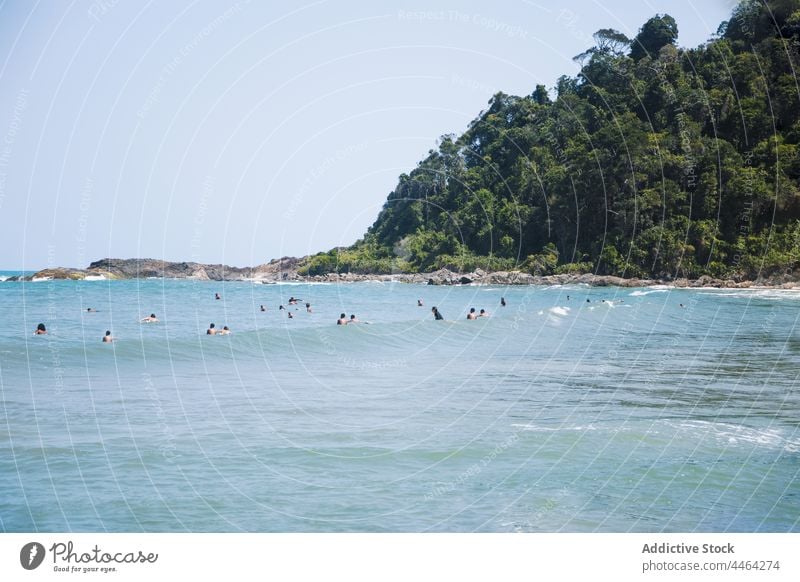Travelers swimming in wavy ocean against mount with trees tourist sky mountain nature landscape highland vacation environment ecology vegetate stormy weather