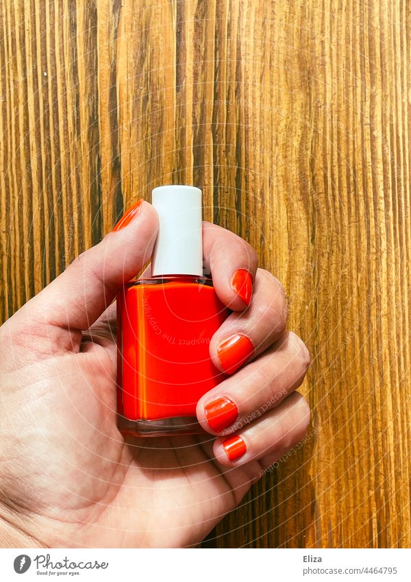 Woman with red painted fingernails holds a bottle with red nail polish Nail polish Red lacquered nails Feminine Manicure Hand Wood stop