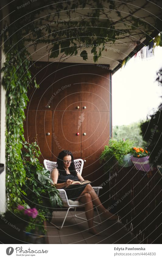 Woman reading a book on a green balcony dreadlocks ivy flowers balcony garden comfortable stay home quarantine resting nature cozy house terrace reading book