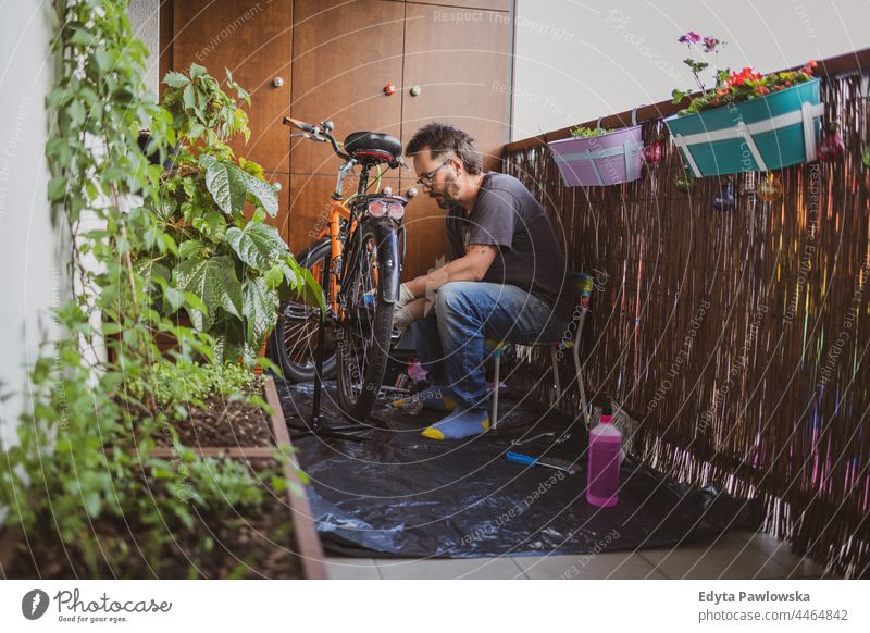 Man fixing his bike on a balcony fixing bike urban nature lifestyle leisure caucasian young city working portrait plant person man male adult diy at home 40s
