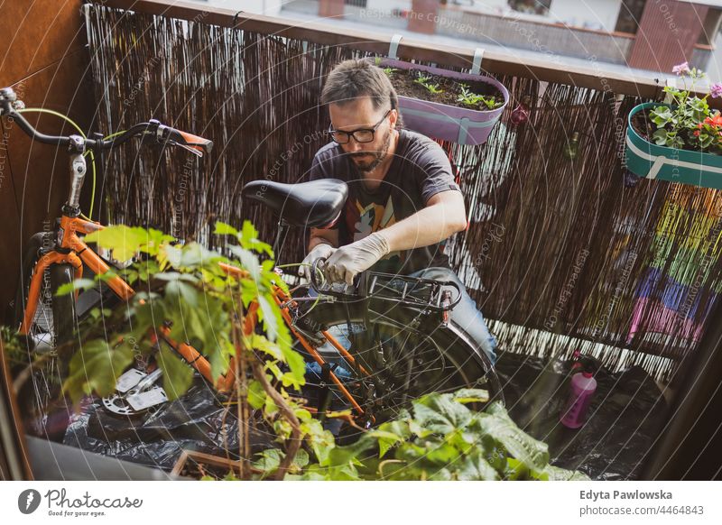 Man fixing his bike on a balcony fixing bike urban nature lifestyle leisure caucasian young city working portrait plant person man male adult diy at home 40s