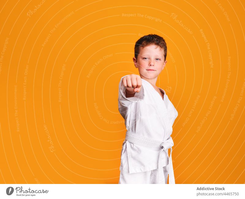 Confident karate boy doing punch in studio confident sport power kimono gaze strong defense kid training fighter serious self assured brave childhood strength