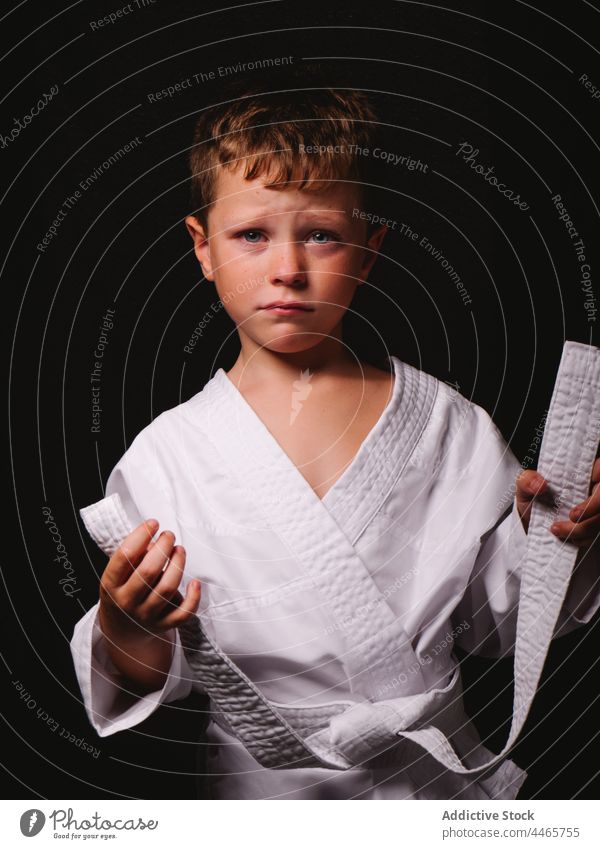 Sad kid in white kimono uniform in studio boy karate expressive child delight carefree individuality appearance childhood cheerful culture content pleasant