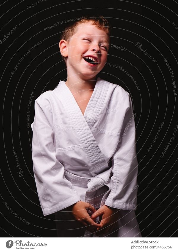 Joyful kid in white kimono uniform laughing in studio boy karate expressive fun joke joy funny mouth opened playful child having fun delight carefree