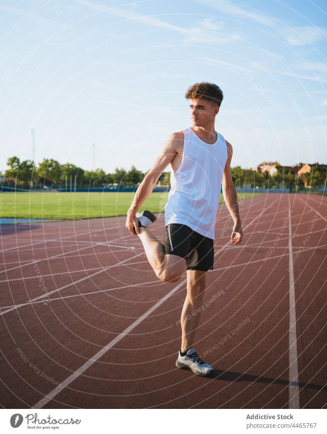 Fit sportsman stretching leg during workout on track athlete leg raised training warm up practice town exercise sneakers sportswear fit cloudy sky wellness