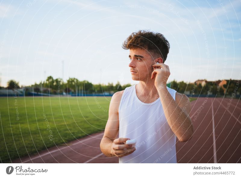 Sportsman listening to song from earbud on track athlete music sport contemplate track and field using gadget device case sportsman sky tws healthy lifestyle