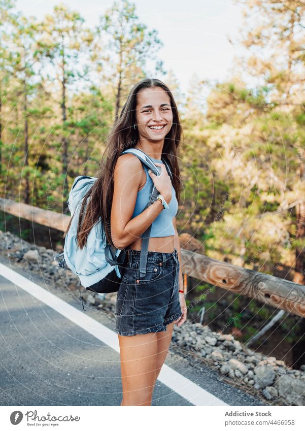 Teen with backpack crossing road against trees traveler nature route attentive environment ecology island teen fence walk asphalt roadway rucksack backpacker