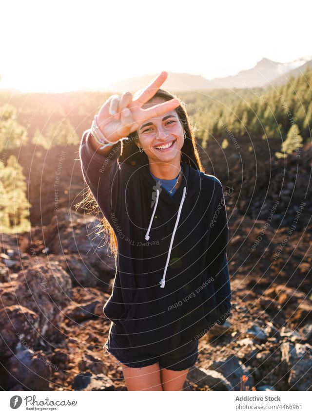 Smiling teenager showing peace gesture against mountain in sunlight smile two fingers victory v sign cool friendly portrait enjoy sincere demonstrate outstretch