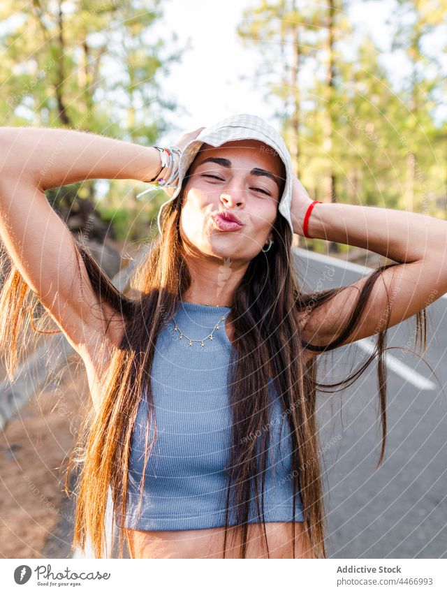 Smiling teen with pouting lips on road teenage hand behind head having fun carefree cool friendly enjoy portrait sincere cheerful panama hat make face weekend