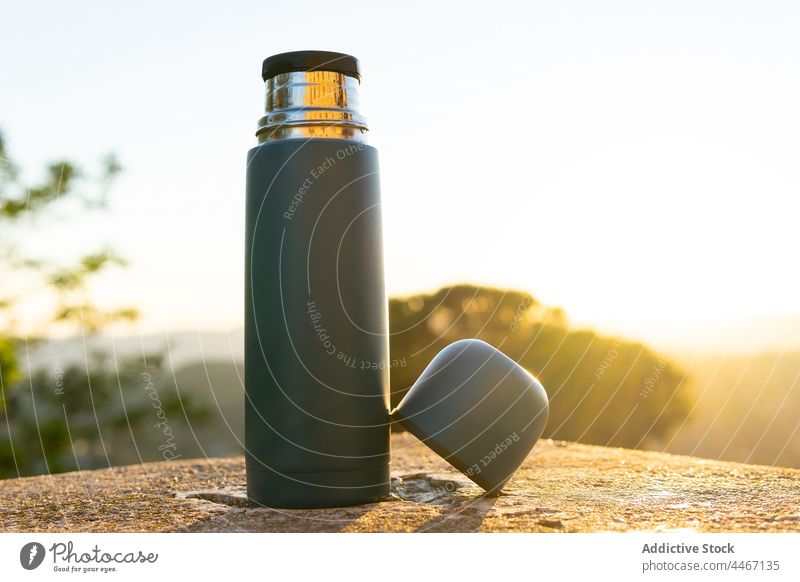 Thermos with cup on stone surface in sunlight thermos design creative modern vacuum flask hot drink sky sunshine beverage plastic sunset shiny bright reflect