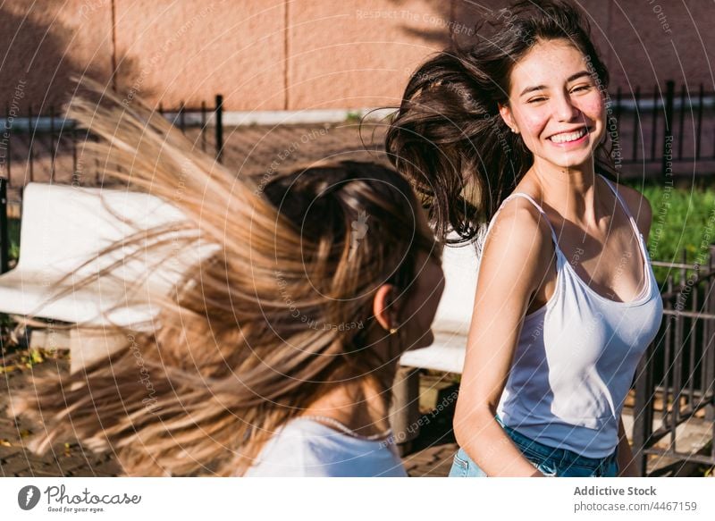 Happy girlfriends with flying hair having fun on street carefree cheerful friendship spend time interact weekend teen energy dynamic active happy toothy smile
