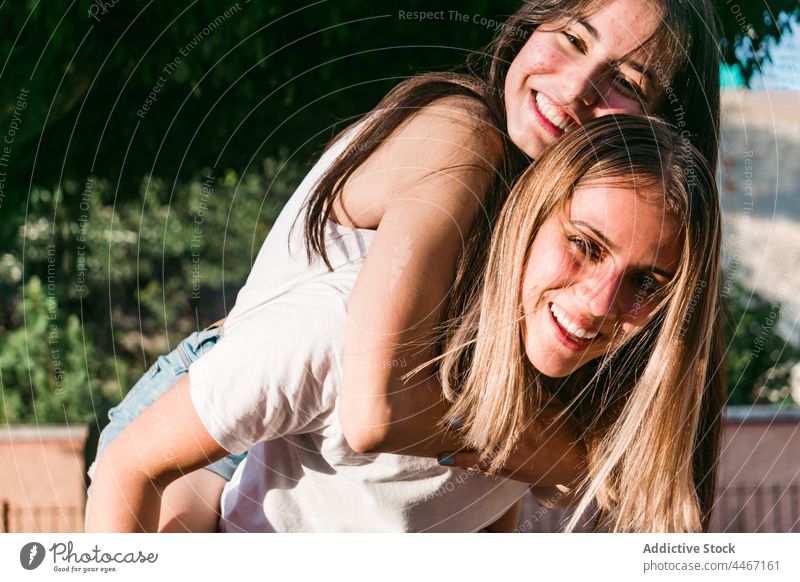 Smiling teen carrying crop girlfriend piggyback on street cheerful having fun friendship embrace spend time carefree portrait weekend bonding best friend