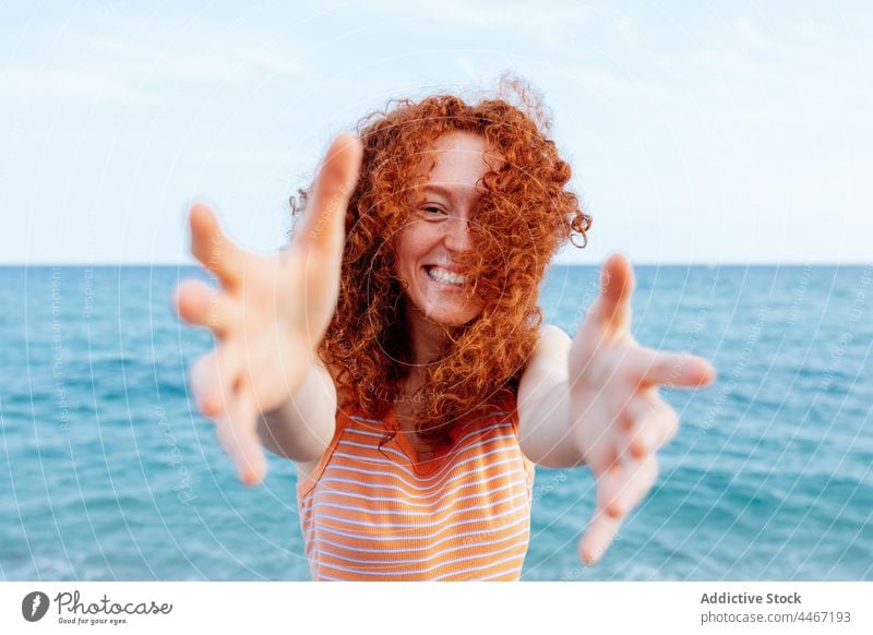 Cheerful woman reaching hands on seashore happy blue wind glad vacation holiday delight female reach out cheerful long hair redhead water nature optimist