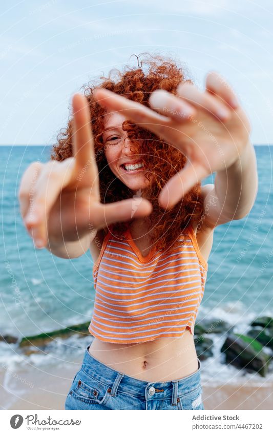 Smiling woman showing triangle gesture near sea coast shape positive happy holiday enjoy female seashore stone curly hair boulder long hair appearance nature