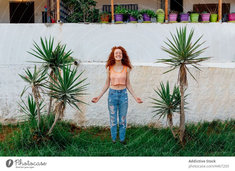 Happy woman standing on grass between palms meditate zen gesture happy carefree exotic enjoy lawn female cheerful optimist toothy smile tree delight plant