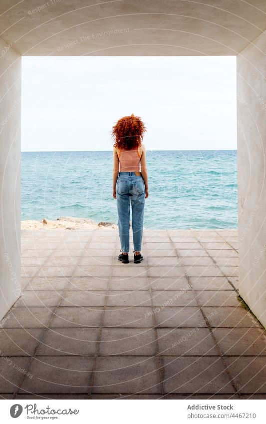 Woman with curly hair standing in concrete hallway on seashore woman traveler blue trip admire passage vacation holiday female nature coast tourist tourism