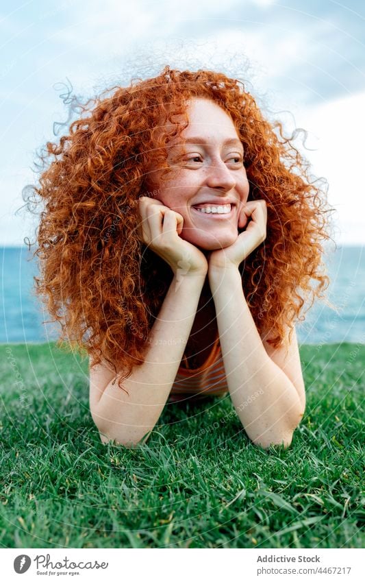 Cheerful ginger haired woman lying on grass happy carefree lawn sea relax expressive freckle female toothy smile young curly hair nature positive glad satisfied