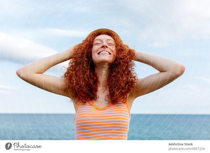 Carefree woman putting hat on head put on carefree travel vacation sea freedom trip holiday female eyes closed tourism curly hair redhead red hair happy enjoy
