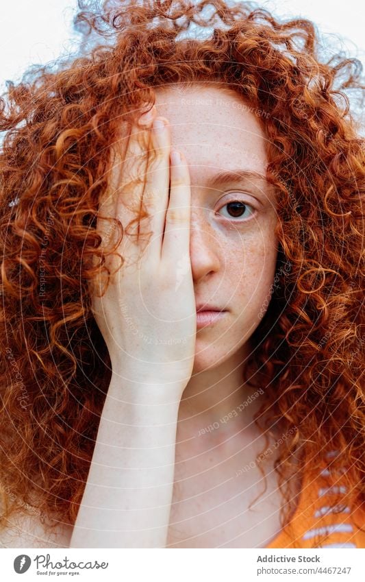 Serious woman covering face with hand portrait freckle feature redhead appearance individuality gaze stare personality female cover eyes human face millennial